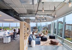 an office space with large windows and lots of furniture on the floor, along with people working at their desks