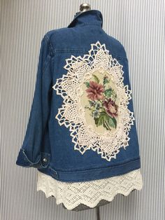 a blue jean jacket with white lace and flowers on the back is hanging up against a striped wall