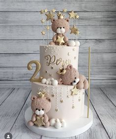 a two tiered cake with teddy bears on top and stars around the edges, sitting on a wooden table