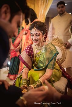 a woman in a green and yellow sari smiles as she sits on the ground