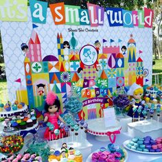 a table topped with lots of cakes and cupcakes next to a sign that says it's a small world