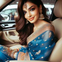 a woman sitting in the back seat of a car wearing a blue sari and gold jewelry