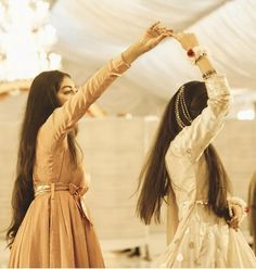 two young women dressed in old fashioned clothing dancing with their hands up to the ceiling