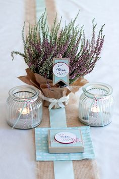 a table topped with jars filled with purple flowers and candles next to a napkin on top of a white table cloth