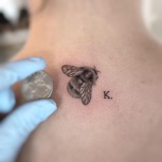 a bee tattoo on the back of a woman's left shoulder is shown next to a coin