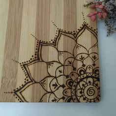 a wooden cutting board with an intricate design on the surface next to a flower arrangement