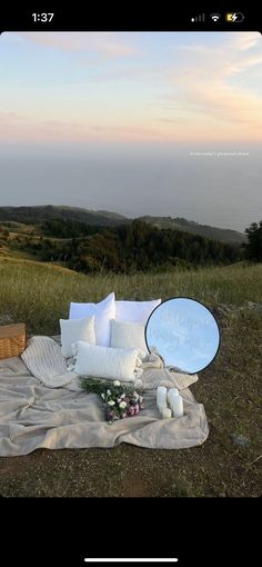 a blanket with pillows and flowers on it in the middle of a grassy field at sunset