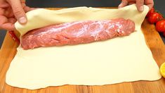 a raw piece of meat is being prepared on a cutting board next to tomatoes and lemons