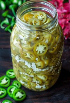 pickled jalapenos in a jar on a table next to green peppers