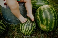 a baby sitting on top of a bucket next to watermelons