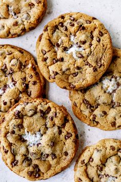 chocolate chip cookies with marshmallows are arranged on a white countertop, ready to be eaten