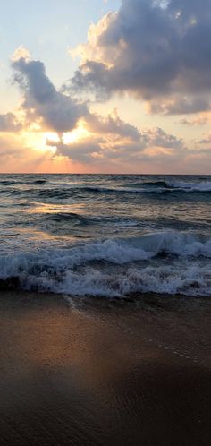 the sun is setting over the ocean with waves crashing on the shore and clouds in the sky