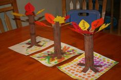 three paper trees with leaves on them sitting on top of napkins in front of a wooden table