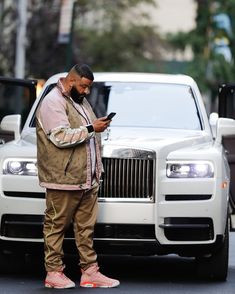 a man standing in front of a white car looking at his cell phone while wearing pink shoes