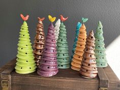 five ceramic christmas trees are lined up on a wooden box with birds perched on them