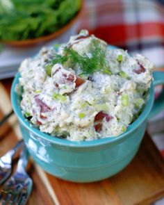 a blue bowl filled with potato salad on top of a wooden cutting board next to silverware