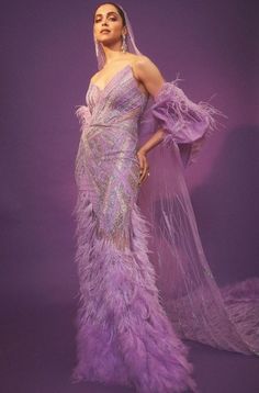 a woman in a purple dress with feathers on her head and veil over her shoulder