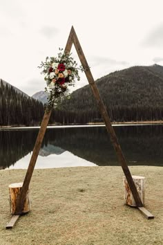 a wedding arch with flowers and greenery on the grass near a body of water