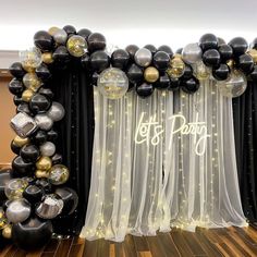 black and gold balloons are on display in front of a curtained backdrop that says let's party