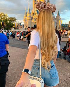 a woman with long blonde hair wearing a mouse ears headband and carrying a white purse