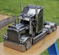 a metal model of a semi - truck on a wooden table in the grass,