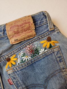 the back pocket of a pair of jeans with daisies on them and a tag attached to it