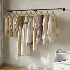 a rack with clothes hanging from it in front of a window and a dresser next to it