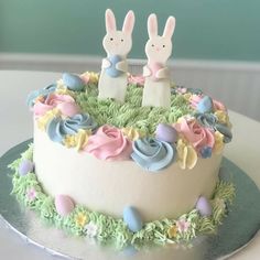 there is a cake decorated with bunnies and flowers on the top, as well as two bunny figurines