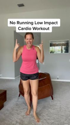 a woman in pink shirt and black shorts standing next to couch with no running low impact cardio workout