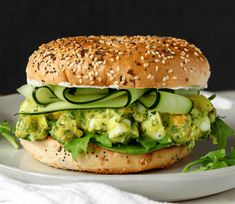 a sandwich with cucumber, lettuce and sesame seeds on a white plate