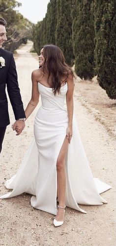 a bride and groom walking down a dirt road holding hands