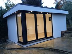 a small white building with black trim and glass doors on the outside, next to some steps