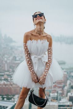 a woman in white dress standing on top of a building with her hands behind her back