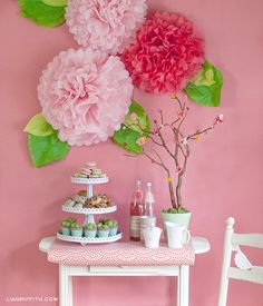 a table topped with pink flowers next to a white vase filled with cupcakes