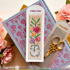 a cross stitch bookmark with scissors and flowers on it next to a pair of scissors