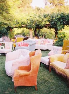 an outdoor seating area with many different colored couches and pillows on the grass in front of trees