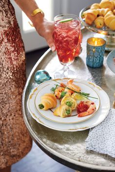 a woman holding a plate with food on it next to a glass of wine and other foods