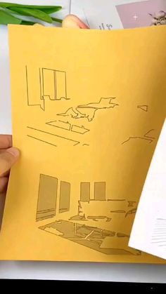 a person holding up a piece of paper that has drawings on it and the pages are yellow