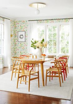 a dining room with floral wallpaper and wooden table surrounded by chairs in front of large windows