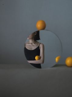 a woman standing in front of a mirror with oranges flying around her