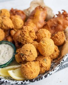 fried food on a plate with lemon wedges and dip in a bowl next to it