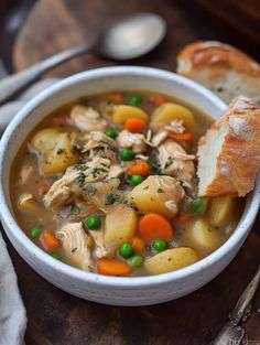 a white bowl filled with chicken and vegetable soup next to a piece of bread on top of a cutting board