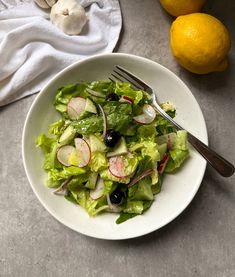 a white bowl filled with salad next to two lemons