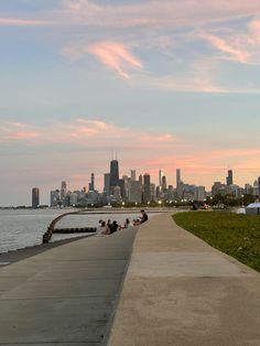 some people are sitting on the edge of a pier by the water and buildings in the background