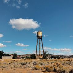 an old rusted water tower in the middle of nowhere with blue skies and clouds