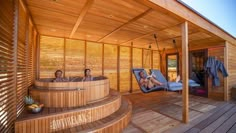 two people sitting in a wooden hot tub on a deck with chaise lounges