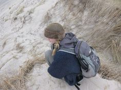 a young boy sitting on top of a sandy beach next to a dog in a backpack