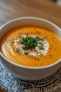 Creamy orange soup topped with a dollop of cream, parsley leaves, and black pepper in a white bowl. Light Lunch