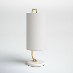 a white table lamp with a gold handle on the base and a white shade over it