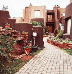 a brick walkway leads to an adobe - style building with potted plants on either side